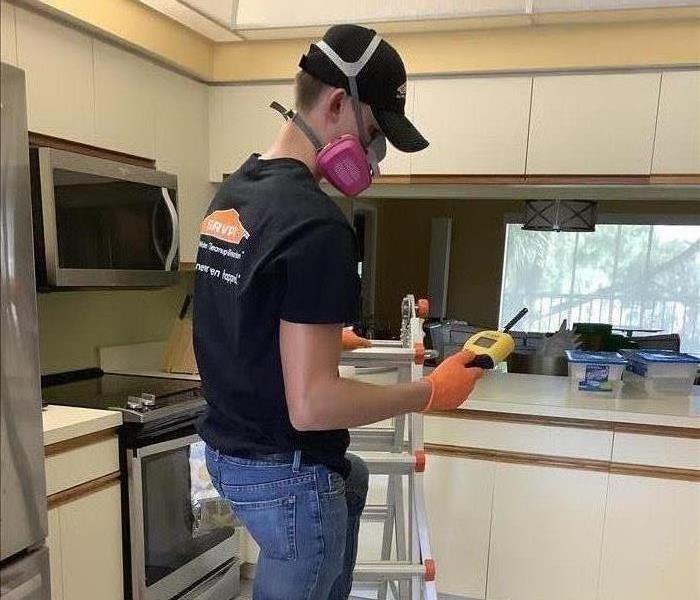 Man on ladder in kitchen with respirator and hygrometer